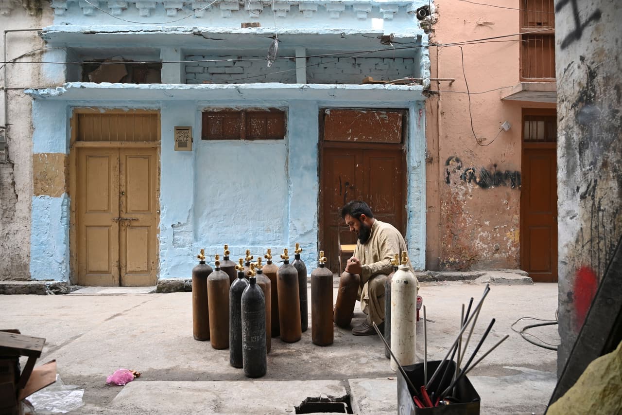 A man kneels in the street cleaning oxygen cylinders