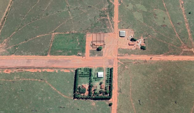 A satellite image of a farm, showing several sheds and a farmhouse at the point where two dirt roads meet in a crossroads. Beyond the small cluster of buildings pasture stretches away in every direction