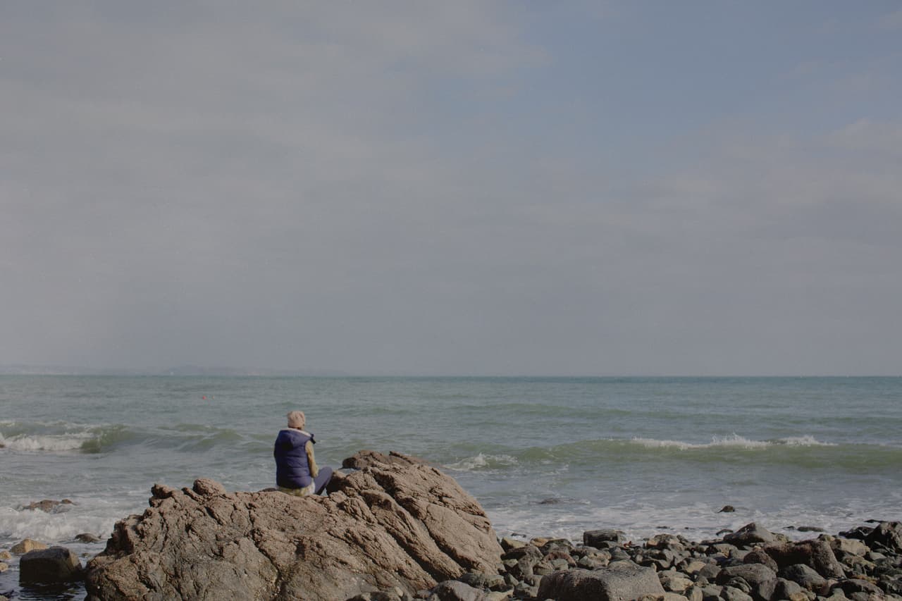 An anonymous woman sits on a rock on the beach