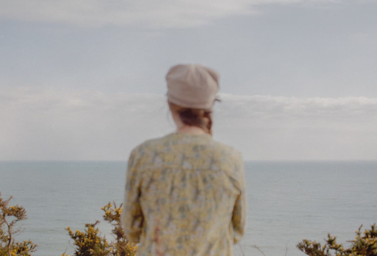 An anonymous woman with her back to the camera looks over the coastline