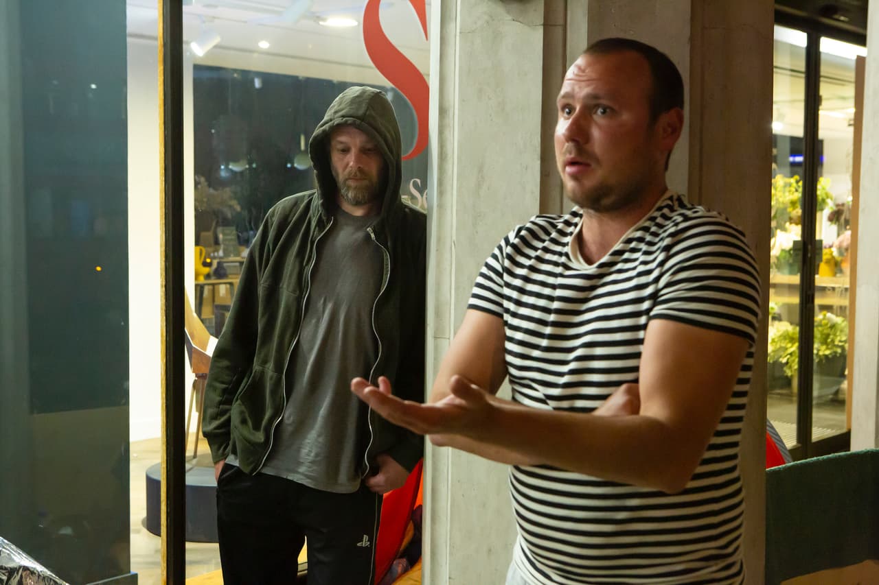 Two men, one in in a hoodie and one in a striped t-shirt, outside the Heals department store