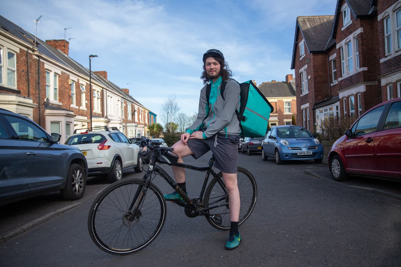 A young man wearing Deliveroo branded gear poses on his bike