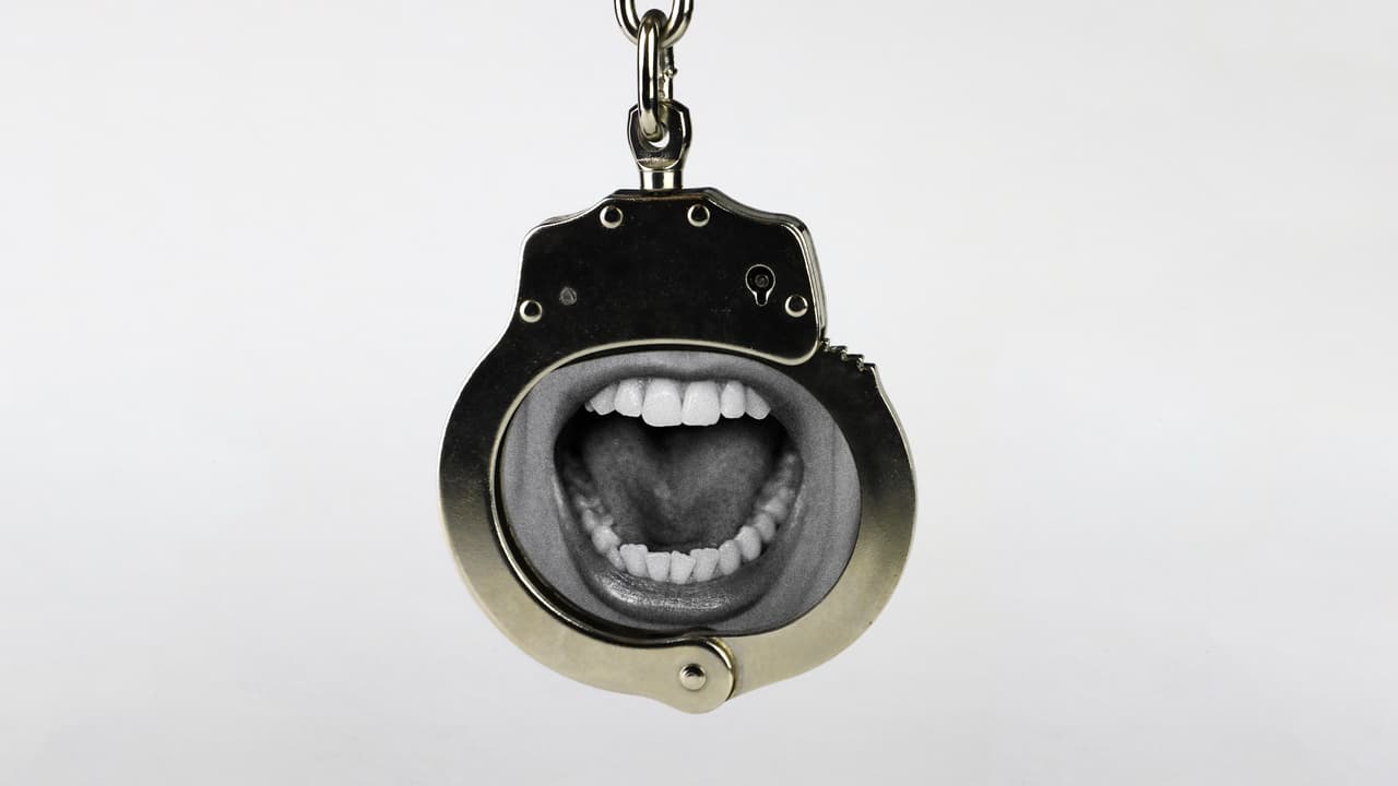 A collage of a single suspended handcuff with a screaming mouth visible through the aperture