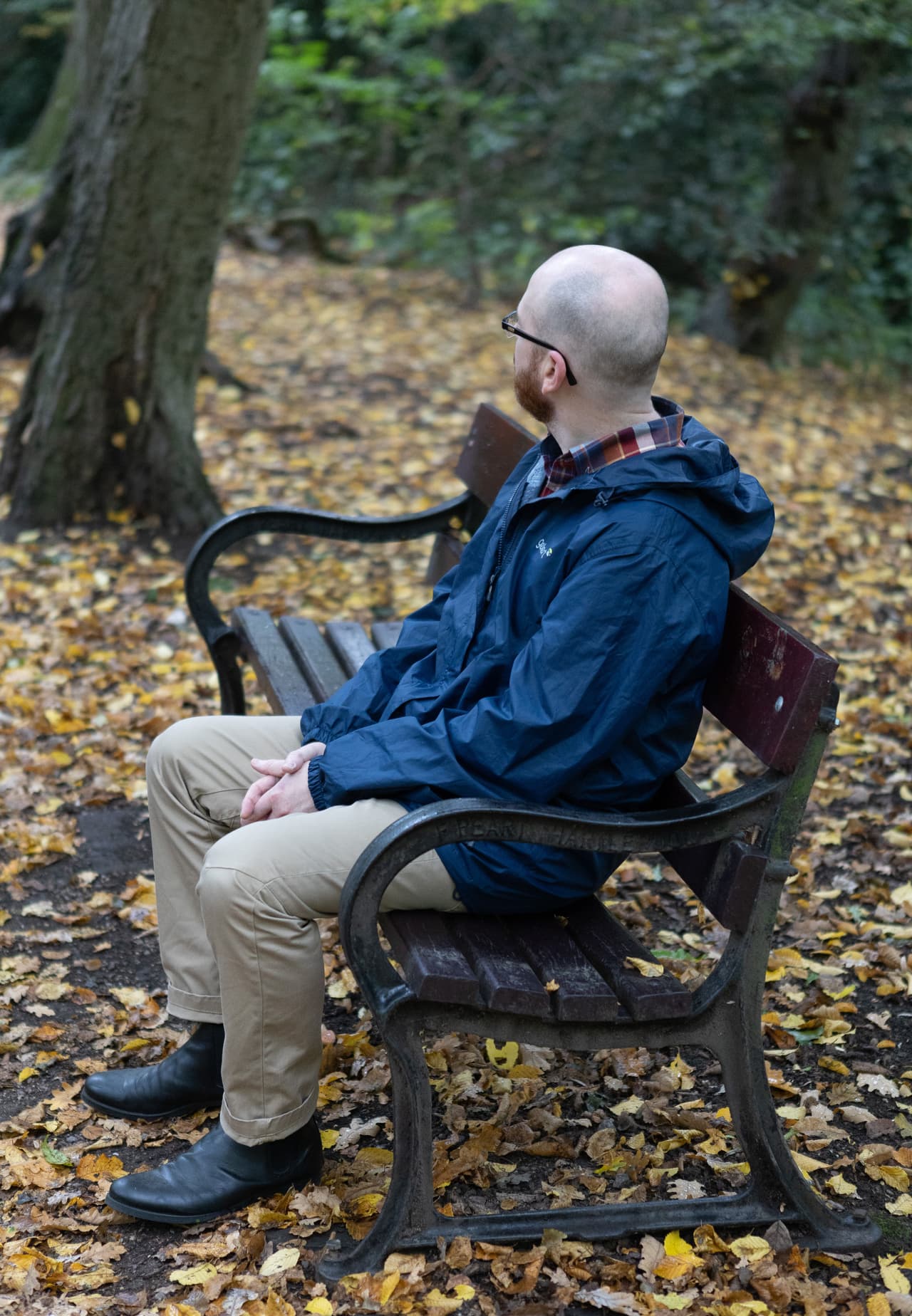 A man sits on a woodland bench with his back turned to the camera