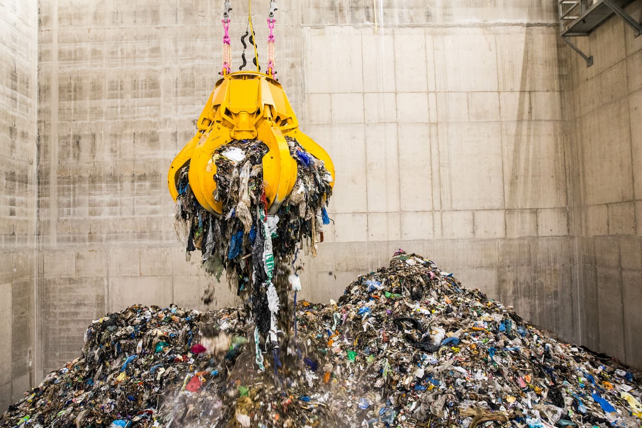 A mechanical claw picking up waste in a landfill