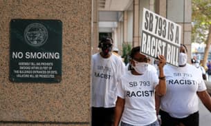 Protestors in white T-shirts with the slogan ‘Say No to SB 793’ walk past a No Smoking sign. One of the protestors carries a sign that says ‘SB 793 is a racist law’
