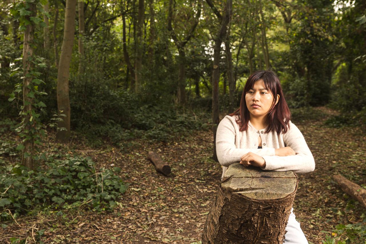 Julia Quecaño Casimiro leans on a tree stump in a wood
