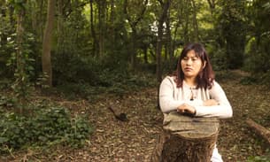 Julia Quecaño Casimiro leans on a tree stump in a wood
