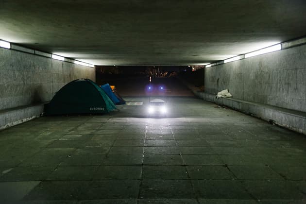 A food delivery robot passes through an underpass of Milton Keynes, near a homeless person's tent, 2018