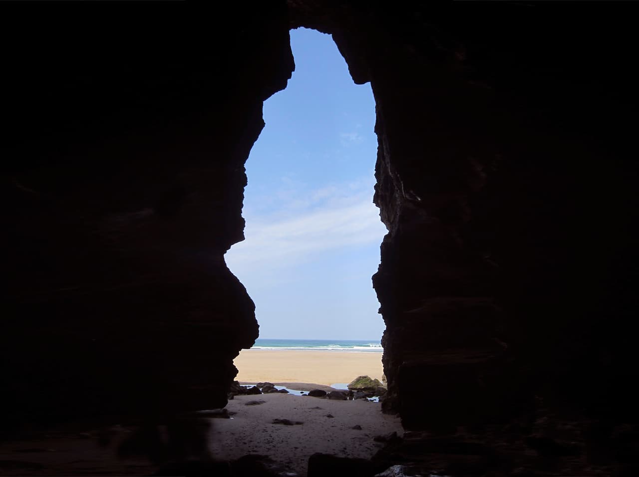The mouth of a cave, showing the sky, sea and a beach beyond