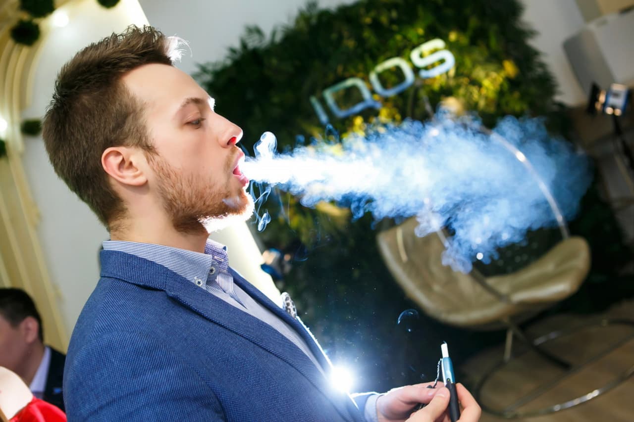 A man using an Iqos blows a stream of smoke