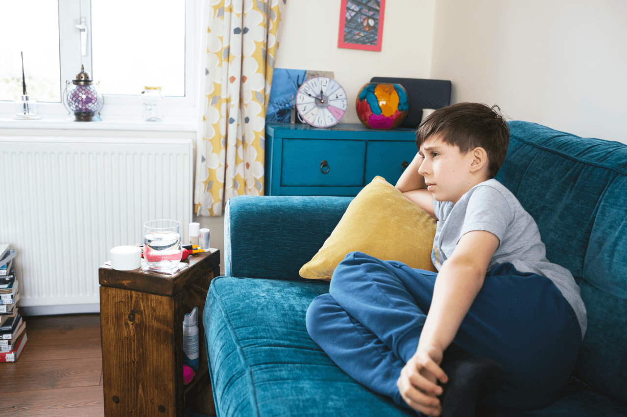 Sam sits on his sofa at home. He no longer goes to school because they couldn’t provide the support he needed