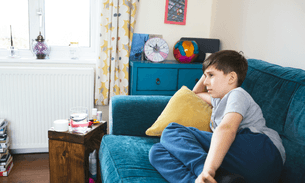 Sam sits on his sofa at home. He no longer goes to school because they couldn’t provide the support he needed