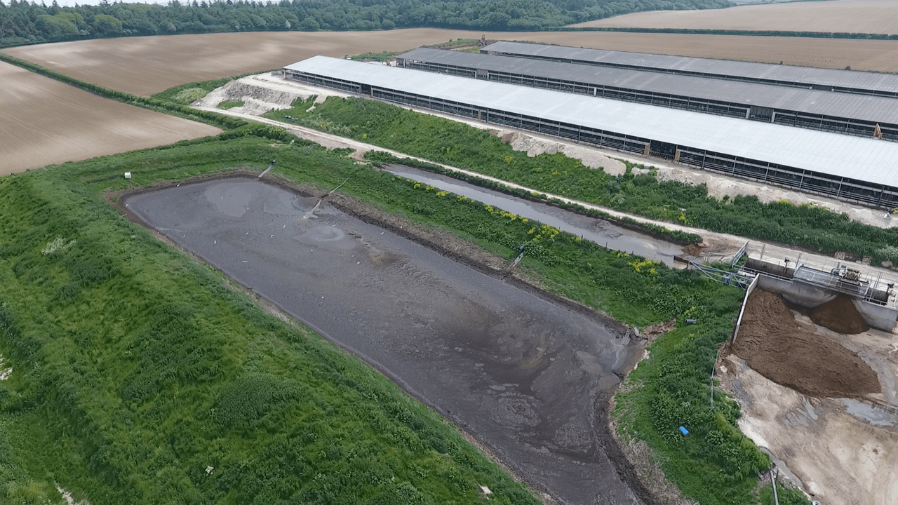 A large rectangular brown slurry lagoon next to a long farm building